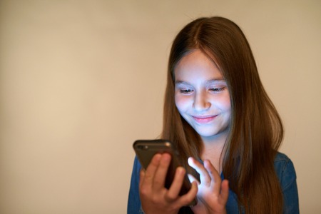 Closeup smiling little girl using smart phone with glowing screen