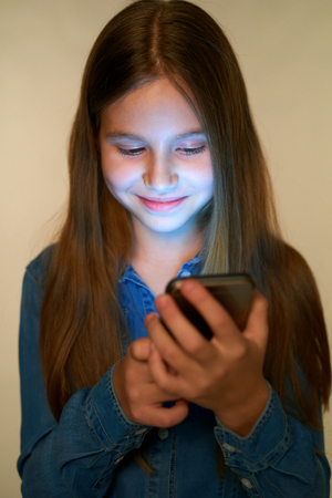 Closeup smiling little girl using smart phone with glowing screenの写真素材