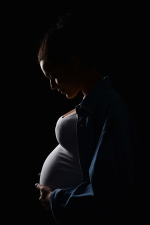 Silhouette of pregnant woman with hands on tummy, profile view, over darkの写真素材