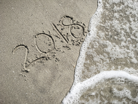 Figures 2018 on wet sand with a wave foam, top viewの写真素材