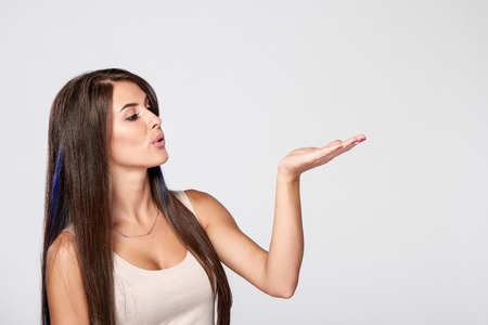 Closeup side view of beautiful brunette woman blowing on palm to the side at blank copy spaceの写真素材