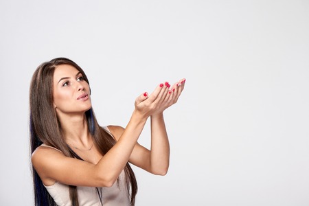 Happy woman with raised hands trying to catch something falling from the above over gray backgroundの写真素材