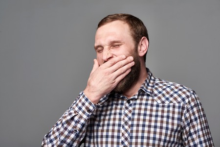 Sleepy young business man in checkered shirt yawning over gray backgroundの写真素材