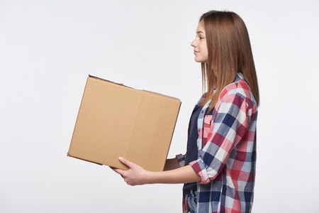 Delivery, relocation and unpacking. Side view portrait of woman giving cardboard box looking forward at blank copy space, isolatedの写真素材
