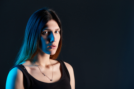 Closeup of young woman on dark background with blue backlitの写真素材