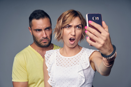 Happy couple in studio laughing making self portrait on smart phone, over grey backgroundの写真素材