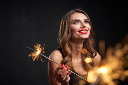 Party, holidays and celebration concept. Closeup of a woman with sparklers in hands looking aside playful happy, over dark backgroundの写真素材