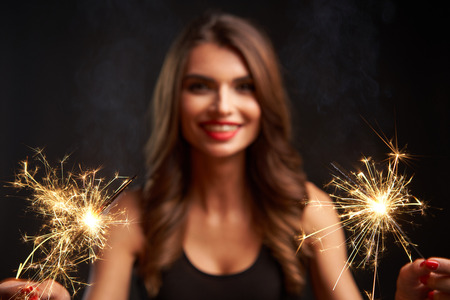Party, drinks, holidays and celebration concept. Woman with sparklers in hands. Shallow depth of field, focus on lightsの写真素材