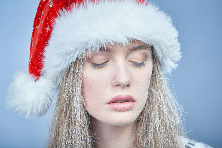 Closeup of sensual frozen girl with snow on face wearing Santa hat looking downの写真素材