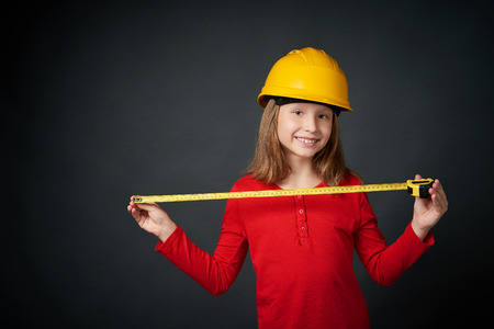 Decoration, renovation and reconstruction concept. Girl wearing construction safety helmet using a measuring tape looking at camera smilingの写真素材