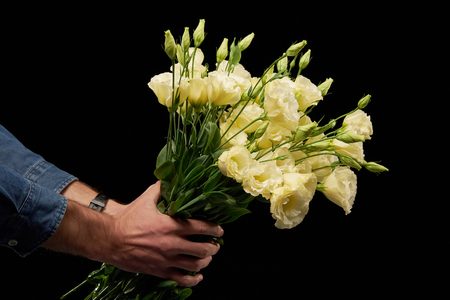 Mans hand presenting a bunch of tender yellow eustoma flowers on black backgroundの写真素材