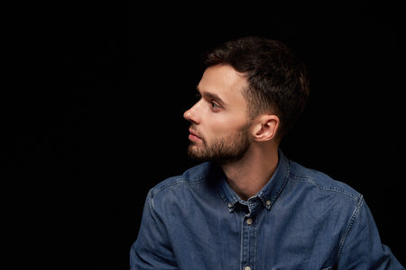 Profile of serious handsome man in denim shirt looking aside at blank copy space, over black backgroundの写真素材