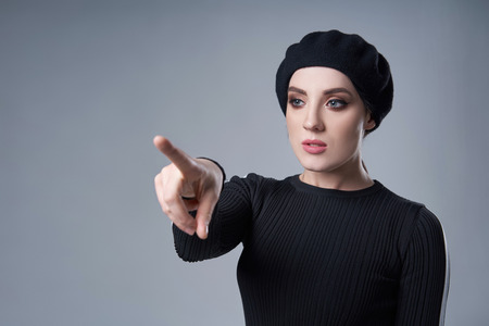 Portrait of a woman wearing beret hat pointing at blank copy space, over gray backgroundの写真素材