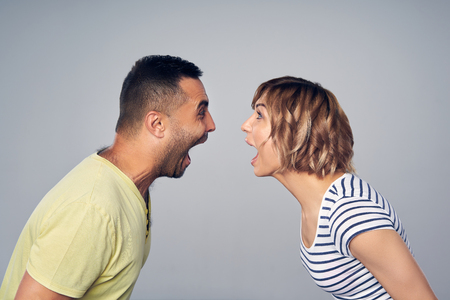 Happy couple screaming of joy looking each at other, over grey backgroundの写真素材
