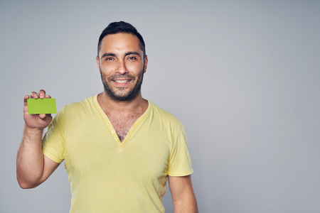 Closeup of casual hispanic man looking at camera and showing blank credit card, studio portrait over gray backgroundの写真素材