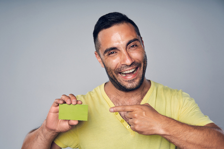 Closeup of happy excited hispanic man looking at camera and showing blank credit card pointing at it, studio portrait over gray backgroundの写真素材