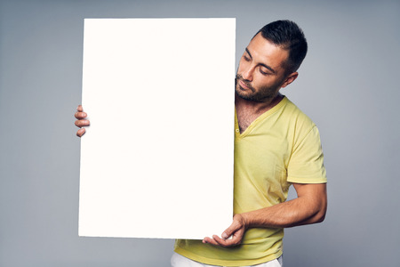 Man holding blank white board with copy space for text, looking at board, over gray backgroundの写真素材