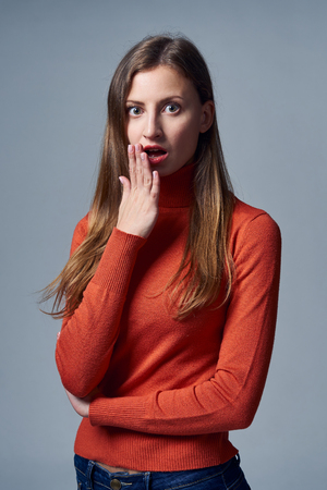 Scared impressed woman with mouth opened covering mouth by palm, over grey backgroundの写真素材