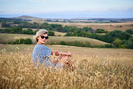 Woman sitting in dry barren grass, looking at camera, smilingの写真素材