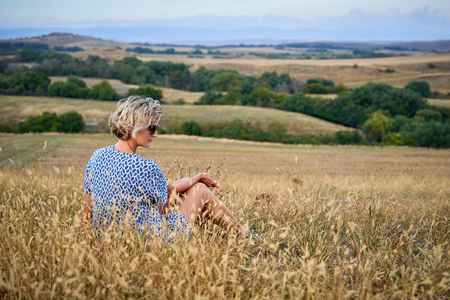 Woman sitting in dry barren grass, looking to side thinking, relaxingの写真素材