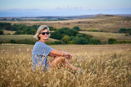 Woman sitting in dry barren grass, looking at camera, smilingの写真素材