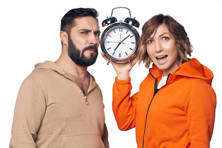 Surprised young couple in home clothes holding big alarm clock over white backgroundの写真素材