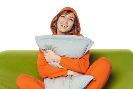 Happy young woman in home clothes sitting on sofa hugging pillowの写真素材