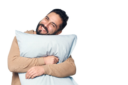 Happy young man in home clothes hugging pillow over white backgroundの写真素材