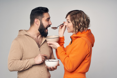 Happy couple in casual clothes eating corn flakes with milk . woman feeding a manの写真素材