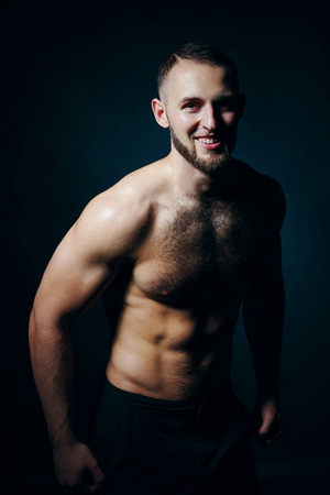 Low key portrait of muscular shirtless man at dark background standing looking at camera smilingの写真素材