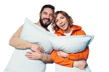 Happy young couple in home clothes hugging pillows over white backgroundの写真素材