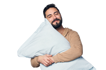 Man in home clothes hugging pillow with closed eyes, over white backgroundの写真素材