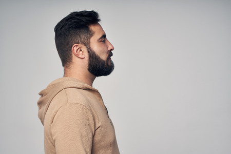 Profile of bearded Hispanic man in casual clothes looking forward, over grey studio backgroundの写真素材