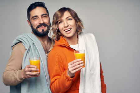 Young couple with towels over shoulder holding glasses of orange juice, isolated on grey backgroundの写真素材