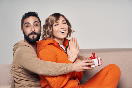 Holiday, celebration and family . Smiling man surprising his girlfriend with present at home sitting on sofaの写真素材
