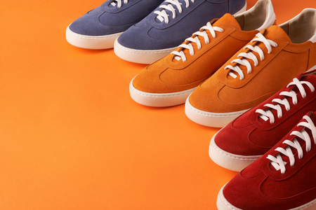 Colorful casual unisex suede sneakers standing in line on orange background with copy space, deep depth of fieldの写真素材