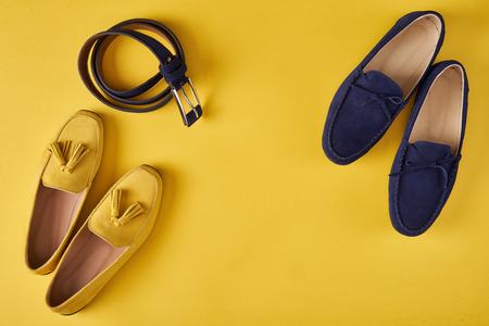Dark blue suede man's and yellow woman's moccasins shoes with a belt over yellow background, top viewの写真素材
