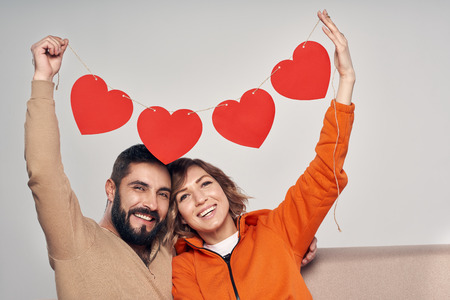 Love and family. Smiling couple sitting on sofa holding four heart shape garlandの写真素材