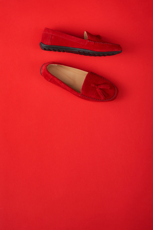 Red suede woman's mocassin shoes over red background, top view with copy spaceの写真素材