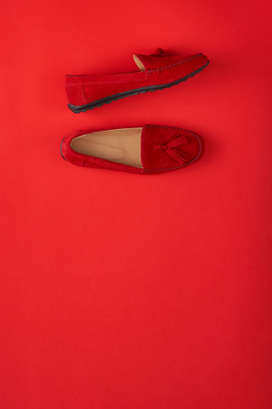 Red suede woman's mocassin shoes over red background, top view with copy spaceの写真素材