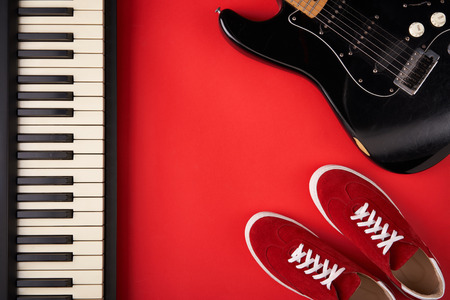 Music band concept. Electric guitar, synthesiser and red stylish sneakers, on red background, flat lay photographyの写真素材
