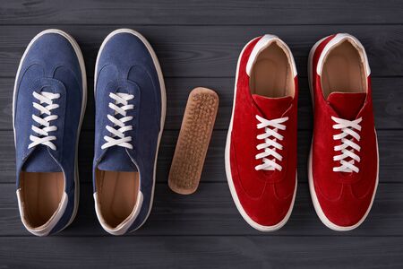 Suede shoes care concept. Top view of red and blue casual unisex suede sneakers with cleaning brush, on grey wooden planksの写真素材
