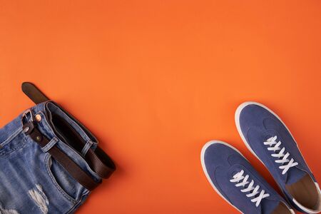 Top view of casual blue suede sneakers on orange background with distressed jeansの写真素材