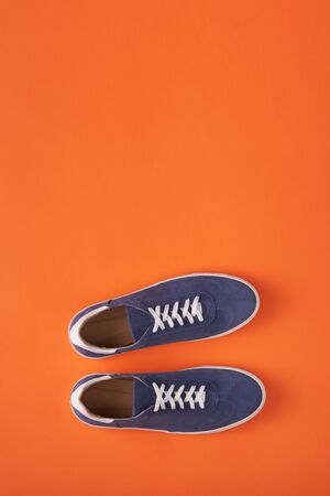 Top view of casual blue suede sneakers on orange background with copy spaceの写真素材