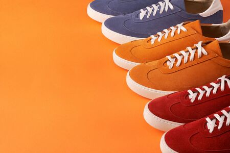 Colorful casual unisex suede sneakers standing in line on orange background with copy space, deep depth of fieldの写真素材