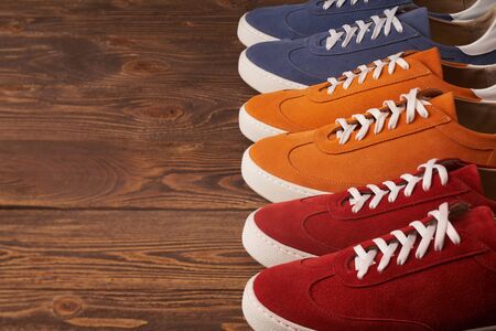 Colorful casual unisex suede sneakers standing in line on brown wooden planks with, copy space, deep depth of fieldの写真素材