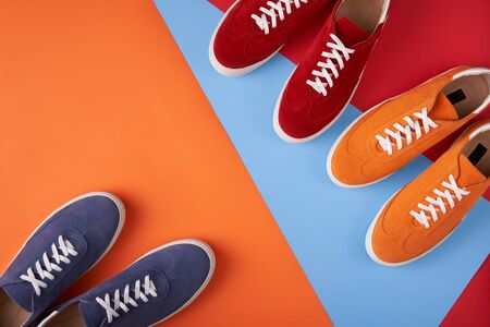Three pairs of colorful casual unisex suede trainers standing on multicolored background, flat lay styleの写真素材