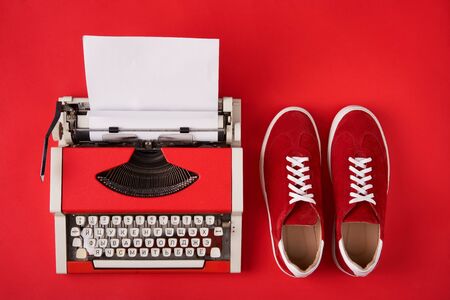 Red suede sneakers shoes and typewriter with blank paper sheet on red background, top view style.の写真素材