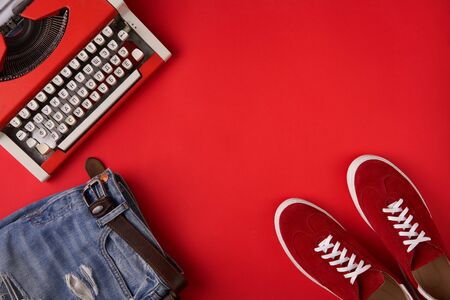 Red suede sneakers shoes, distressed jeans and typewriter on red background, top view style.の写真素材
