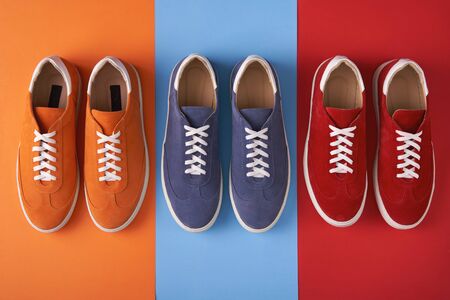 Three pairs of colorful casual unisex suede sneakers standing in line on multicoloured background, flat lay styleの写真素材